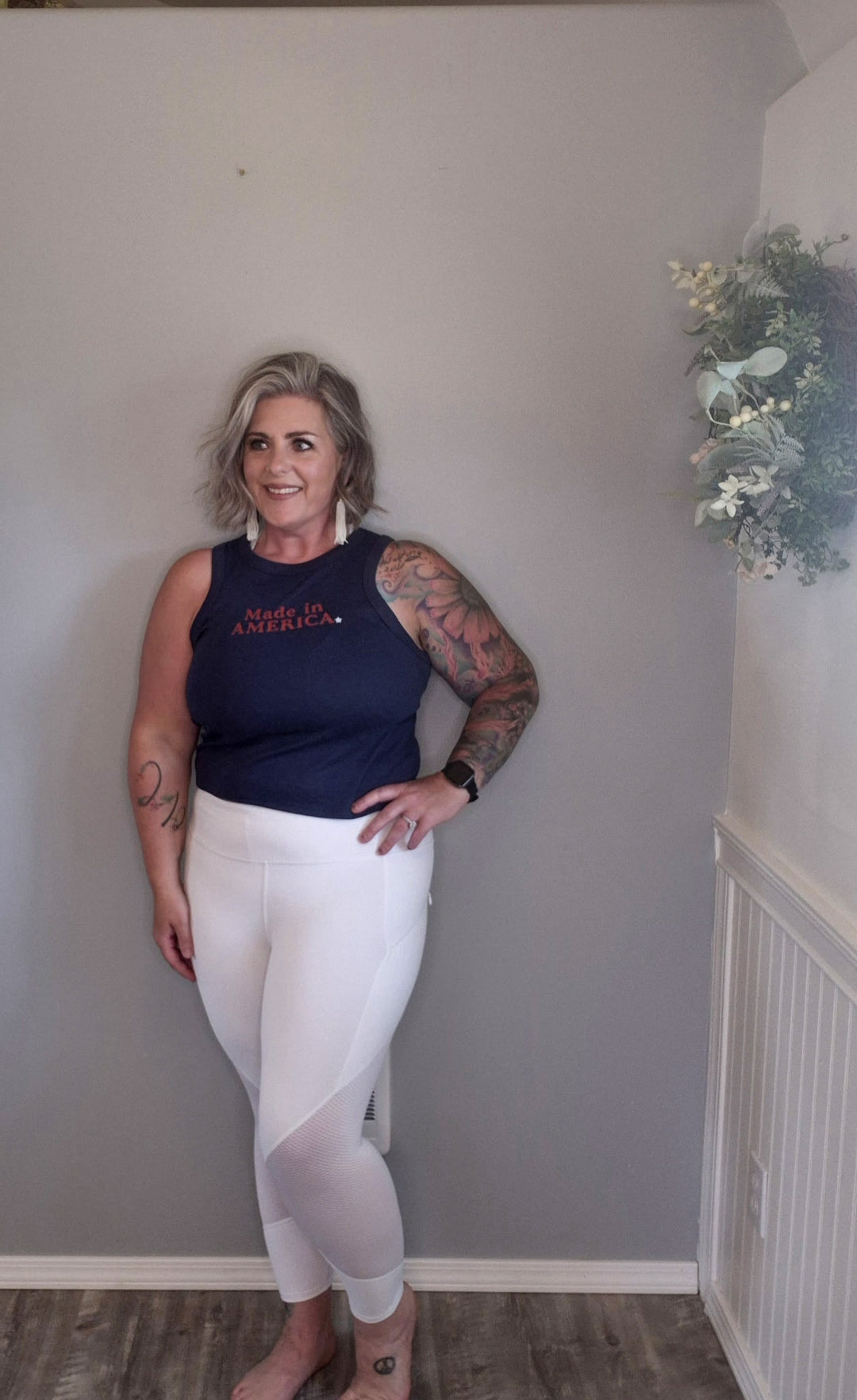 Woman wearing blue tank top that says 'made in America' with a white star. crop cut and styled with white leggings 