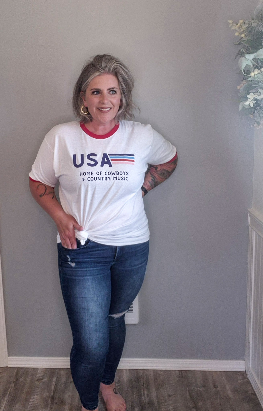 Vintage styled tee with red cuffing around sleeves and neck, 'USA Home of Cowboys and Country Music' with vintage striping in various colors next to USA. Styled with skinny jeans