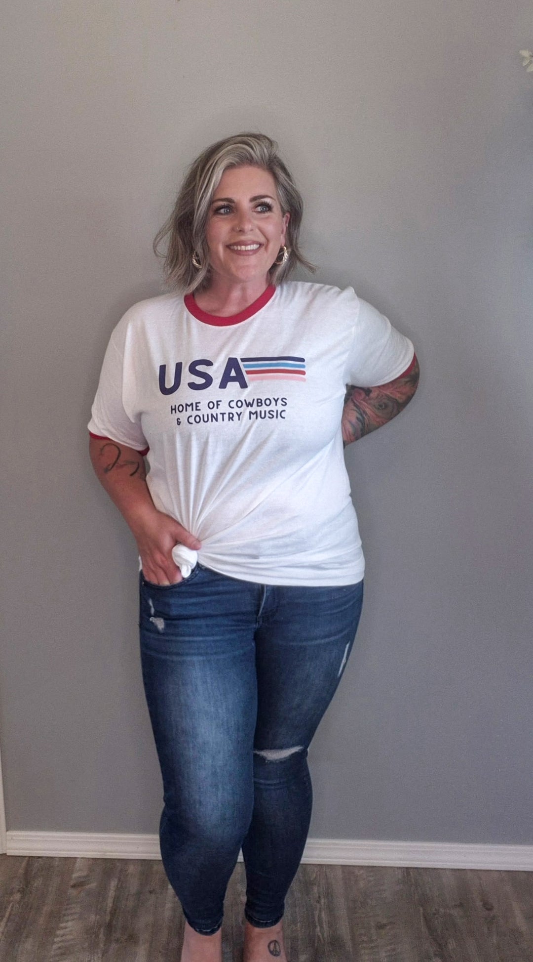 Vintage styled tee with red cuffing around sleeves and neck, 'USA Home of Cowboys and Country Music' with vintage striping in various colors next to USA. Styled with skinny jeans