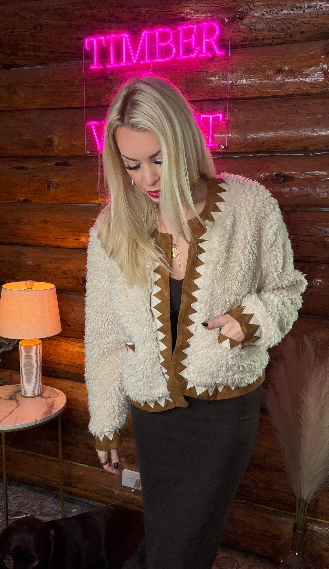 Woman wearing a western style textured jacket in front of a wooden wall with a neon sign.