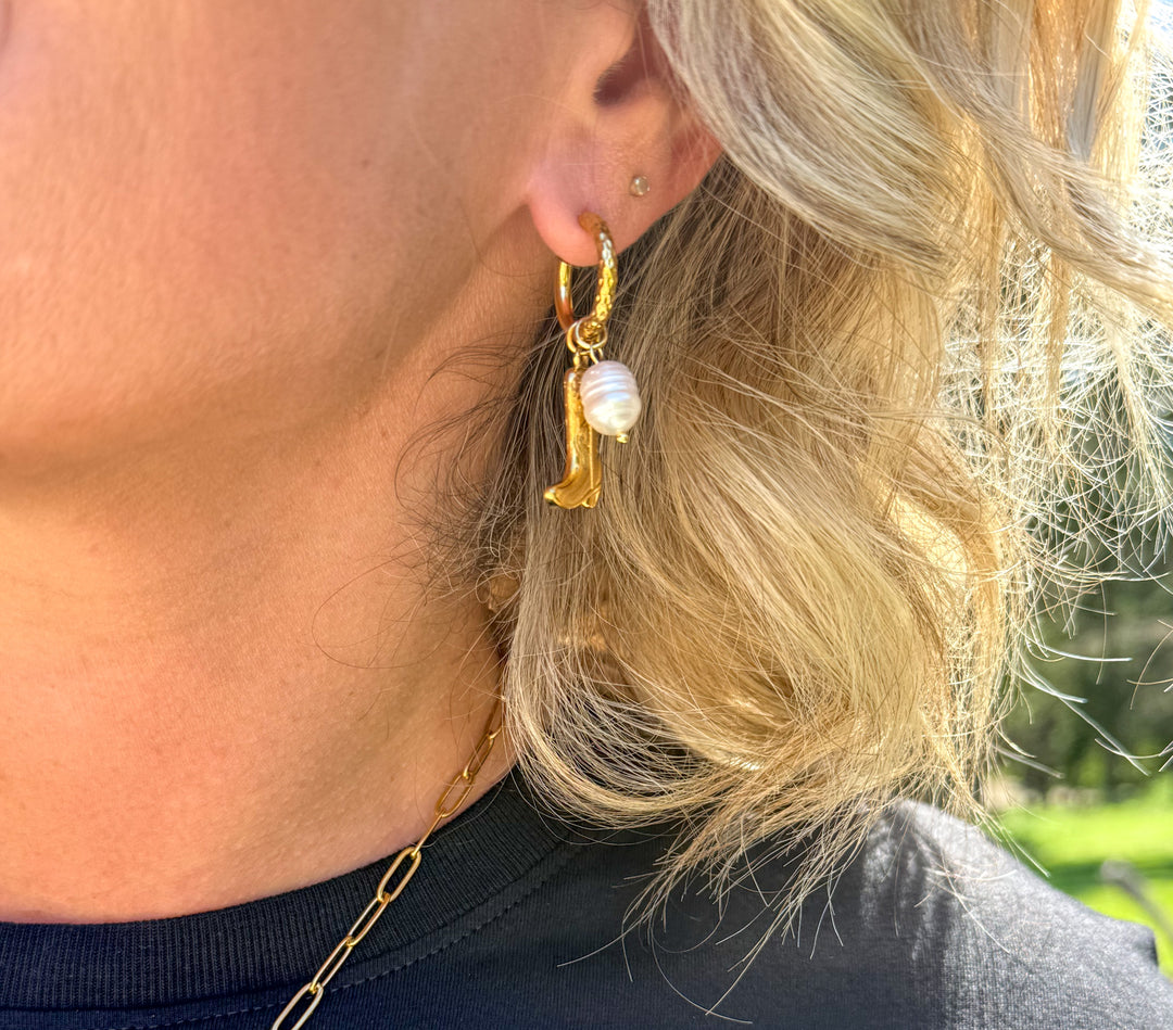 woman wearing gold huge earrings with a cowboy boot and pearl