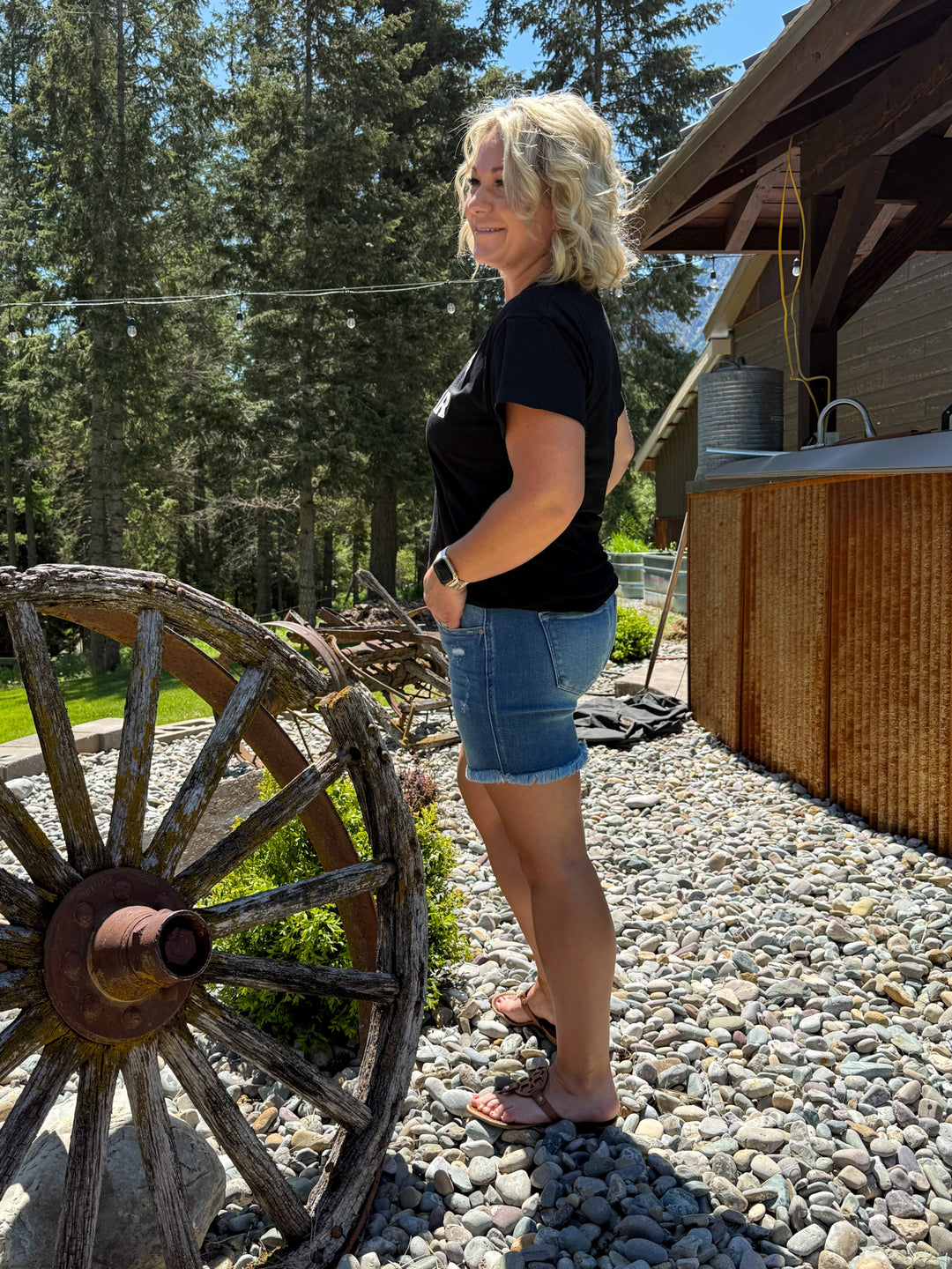 Model wearing KanCan button fly medium wash denim shorts with frayed hem and small amount of distressing 