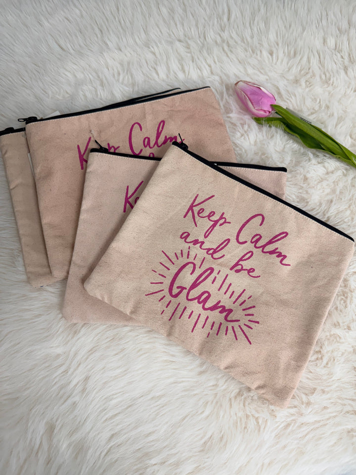 Beige pouches with 'Keep Calm and Be Glam' text on a fluffy white surface.