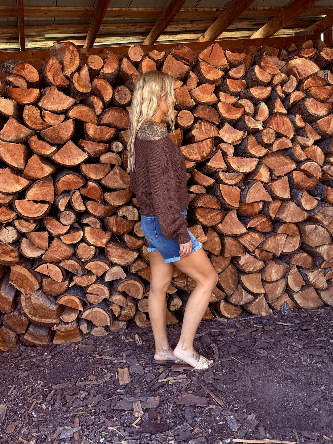 lady wearing chocolate colored open weave off the shoulder sweater with blue jean button fly shorts.