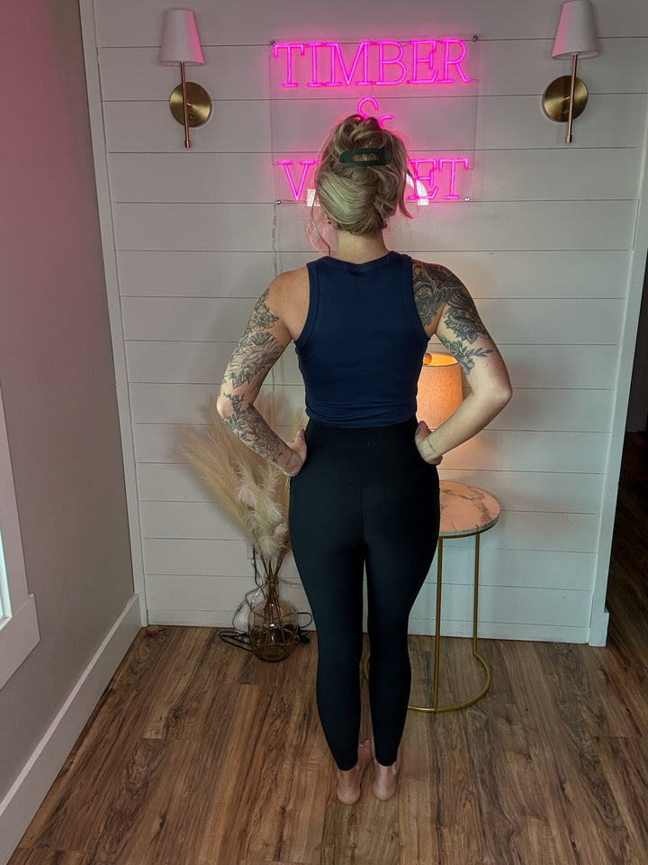 Woman wearing ribbed high compression black leggings with v crossover cut in the front, and a tank top that says 'made in america'