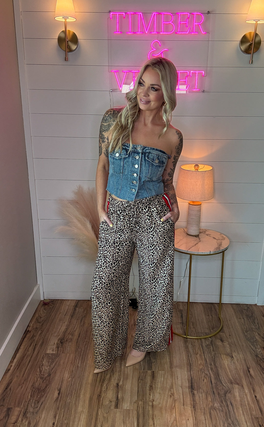 woman wearing denim sleeveless button up corset with two front pockets and with leopard pants and heels 