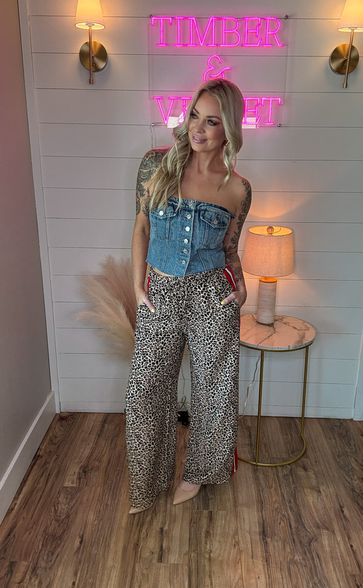 woman wearing denim sleeveless button up corset with two front pockets and with leopard pants and heels 