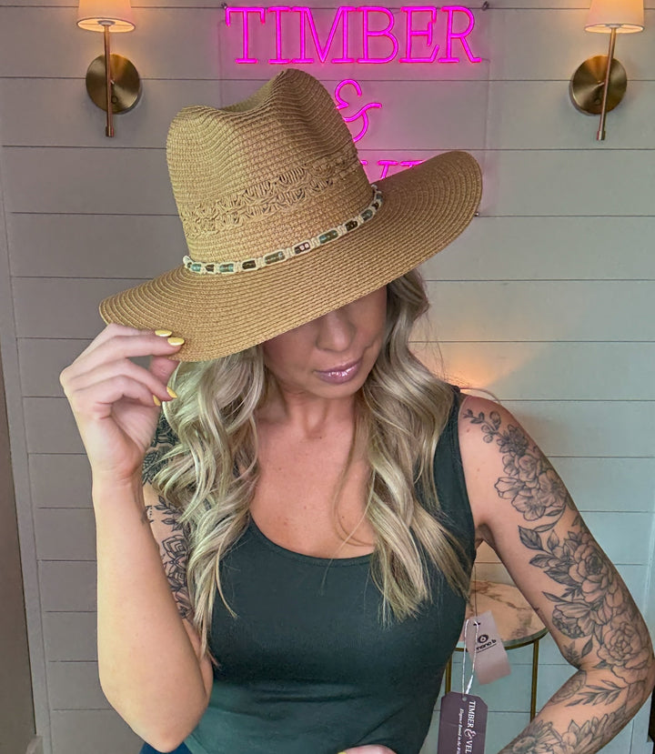 woman wearing a woven cowboy sun hat with beaded detailing and bow tie in the back. 