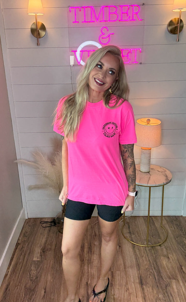 woman wearing bright hot pink graphic tee with expensive, difficult, talks back around a smiley face with black biker shorts 