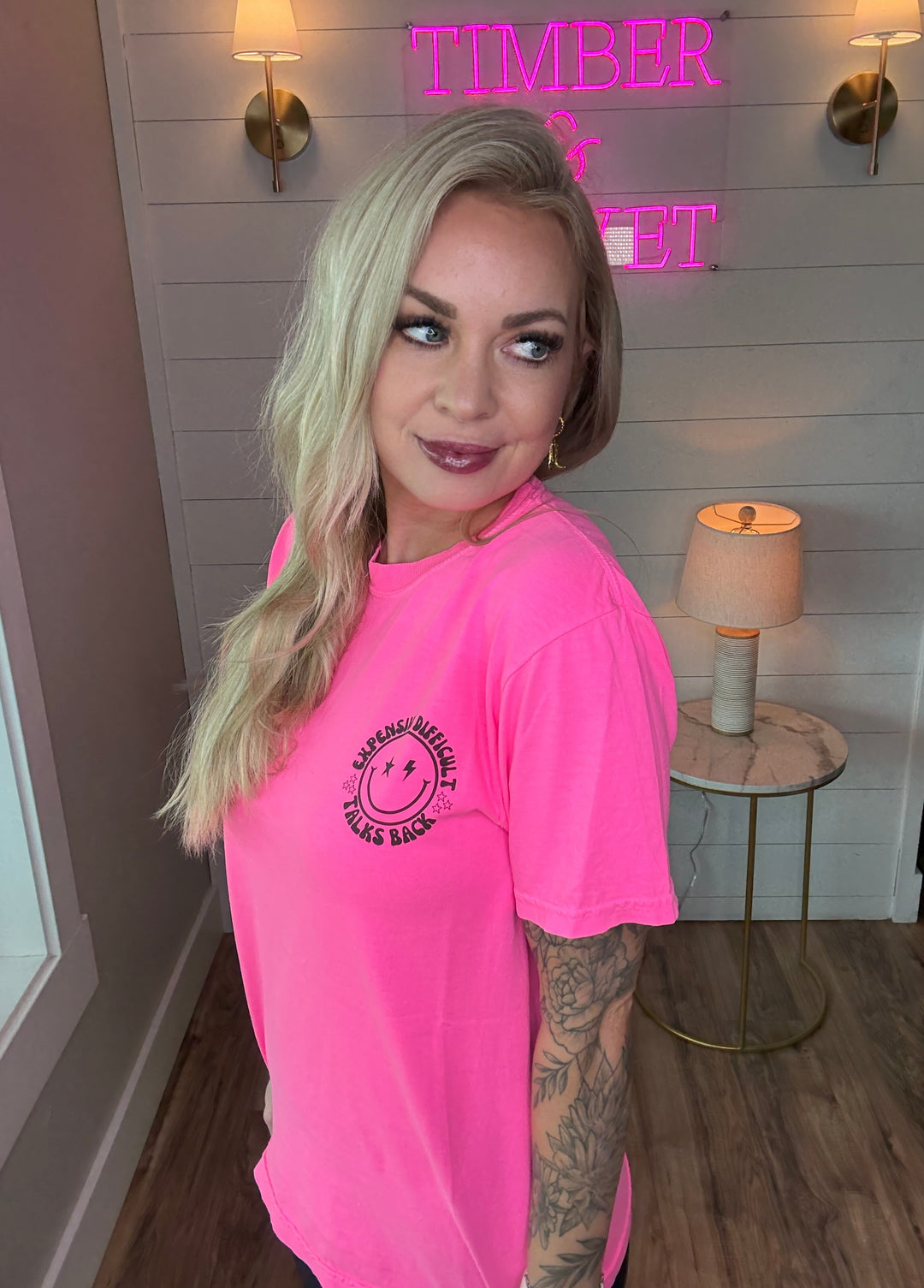 woman wearing bright hot pink graphic tee with expensive, difficult, talks back around a smiley face with black biker shorts 