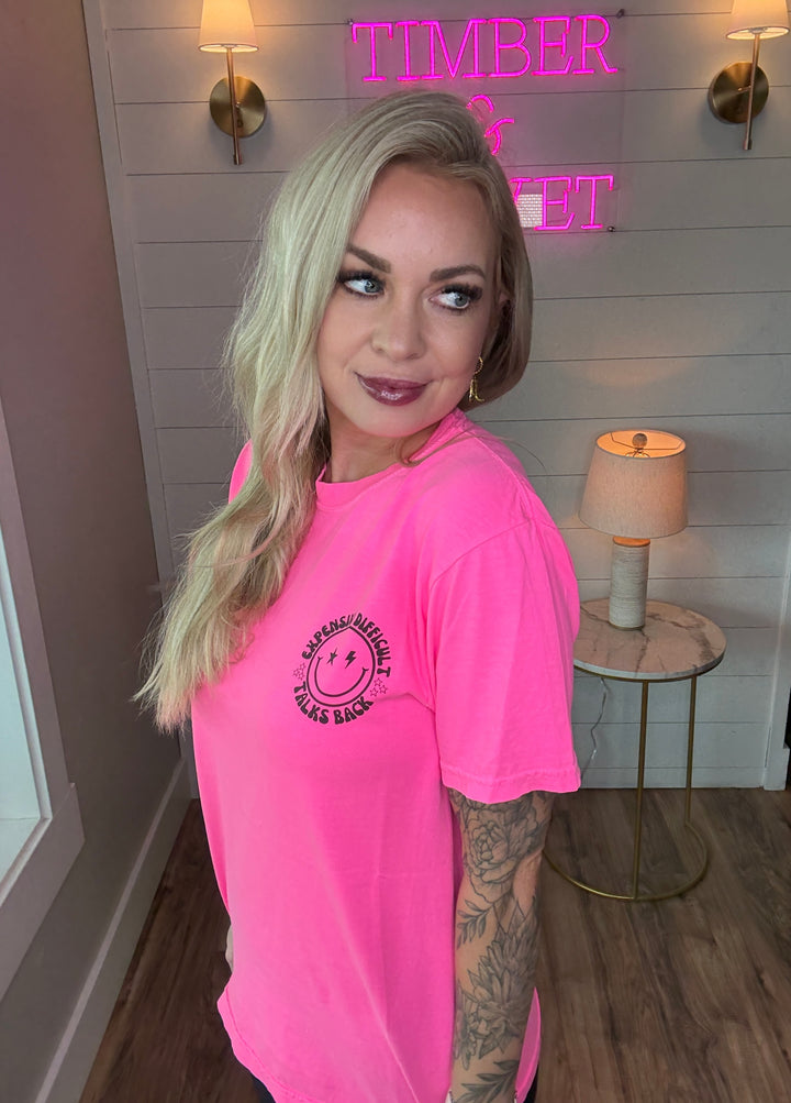 woman wearing bright hot pink graphic tee with expensive, difficult, talks back around a smiley face with black biker shorts 