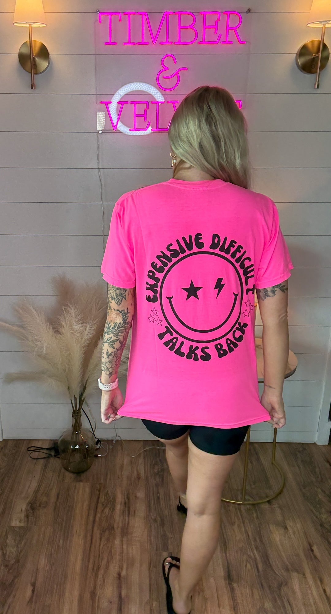 woman wearing bright hot pink graphic tee with expensive, difficult, talks back around a smiley face with black biker shorts 