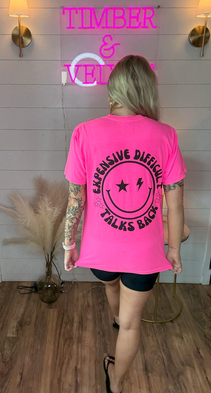 woman wearing bright hot pink graphic tee with expensive, difficult, talks back around a smiley face with black biker shorts 