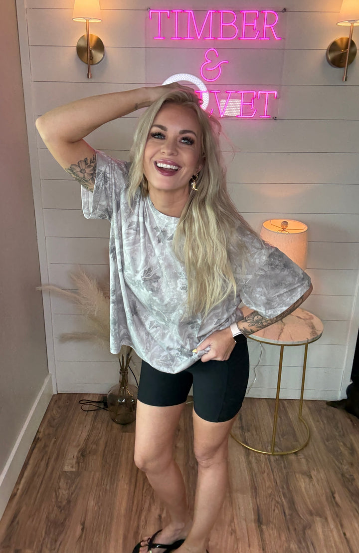 Woman wearing light camo tshirt that is oversized with a pair of black biker shorts 