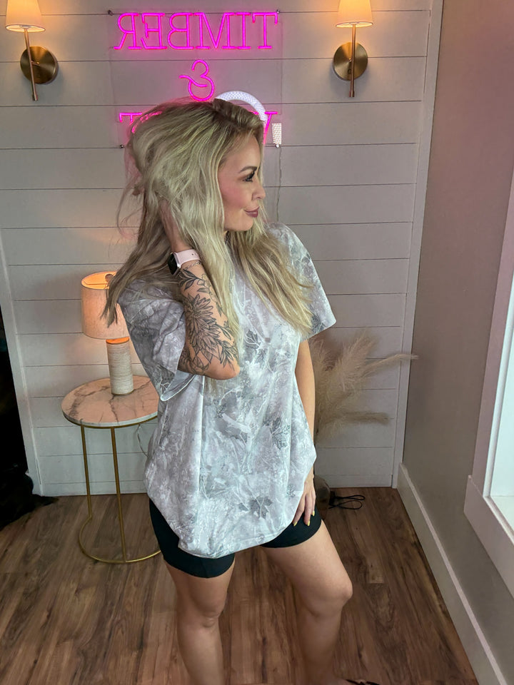 Woman wearing light camo tshirt that is oversized with a pair of black biker shorts 