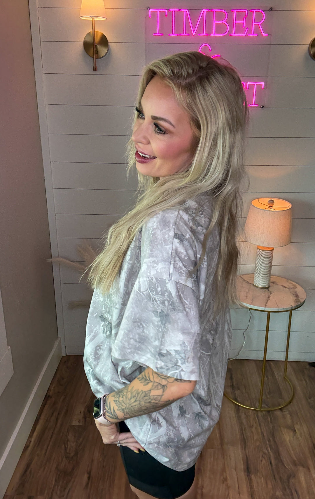 Woman wearing light camo tshirt that is oversized with a pair of black biker shorts 