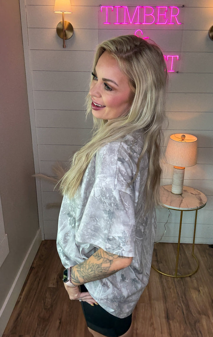 Woman wearing light camo tshirt that is oversized with a pair of black biker shorts 