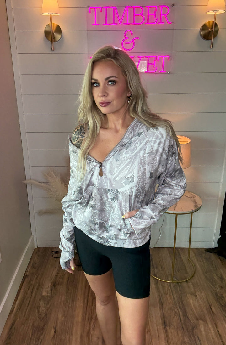 Woman wearing light camo pullover zip hoodie with leather zipper and black biker shorts 
