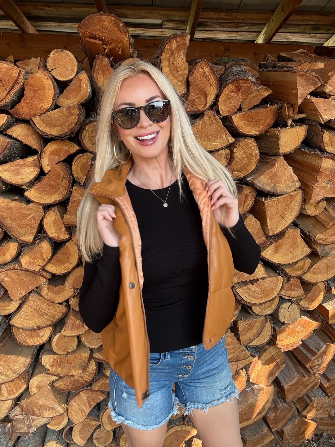Woman wearing a camel faux leather vest standing in front of a wood stack 