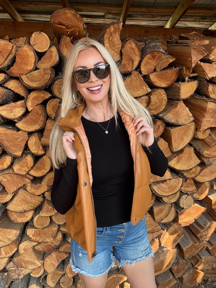 Woman wearing a camel faux leather vest standing in front of a wood stack 