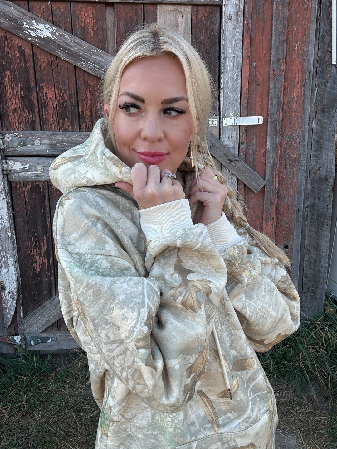 Woman wearing a camo MONTANA hoodie in front of a wooden door.