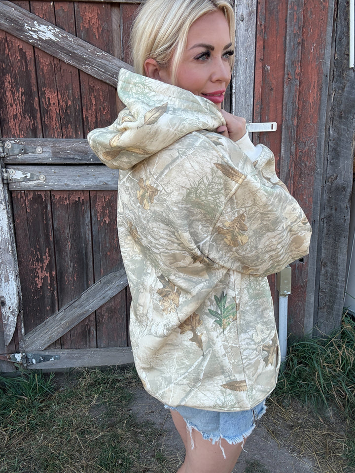 Woman wearing a camouflage Montana Hoodie in front of a wooden fence
