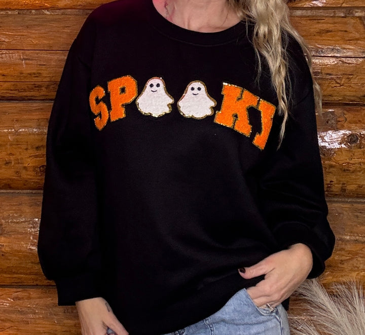 Person wearing a black sweatshirt with 'SPooky' and ghost designs against a wooden background