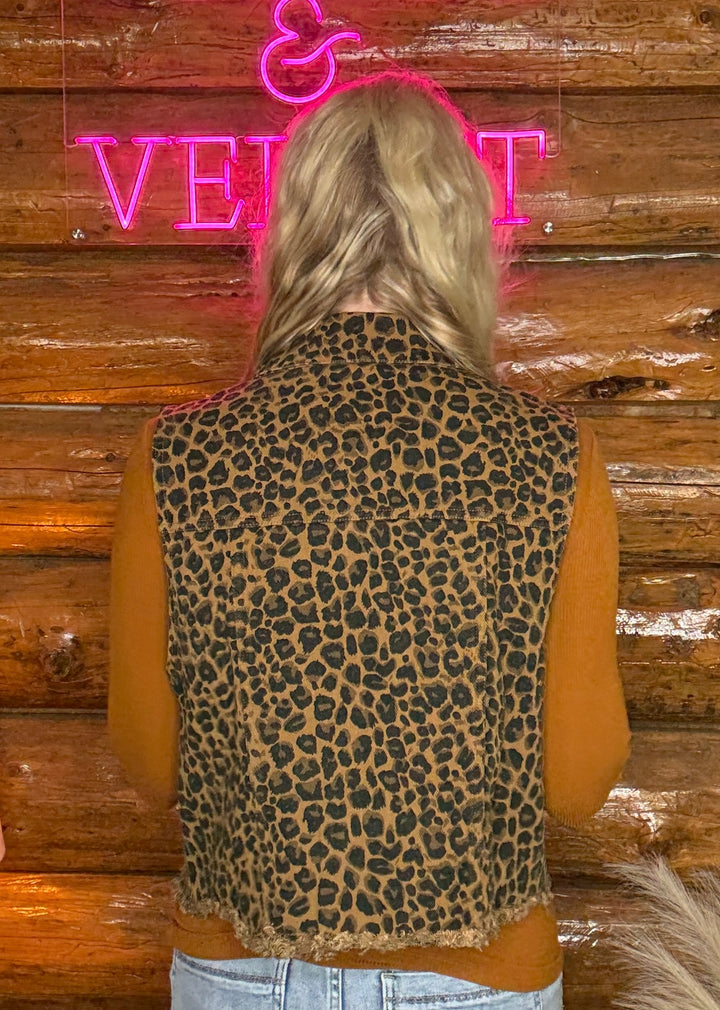 Person wearing a leopard print vest with a wooden wall and pink neon sign in the background