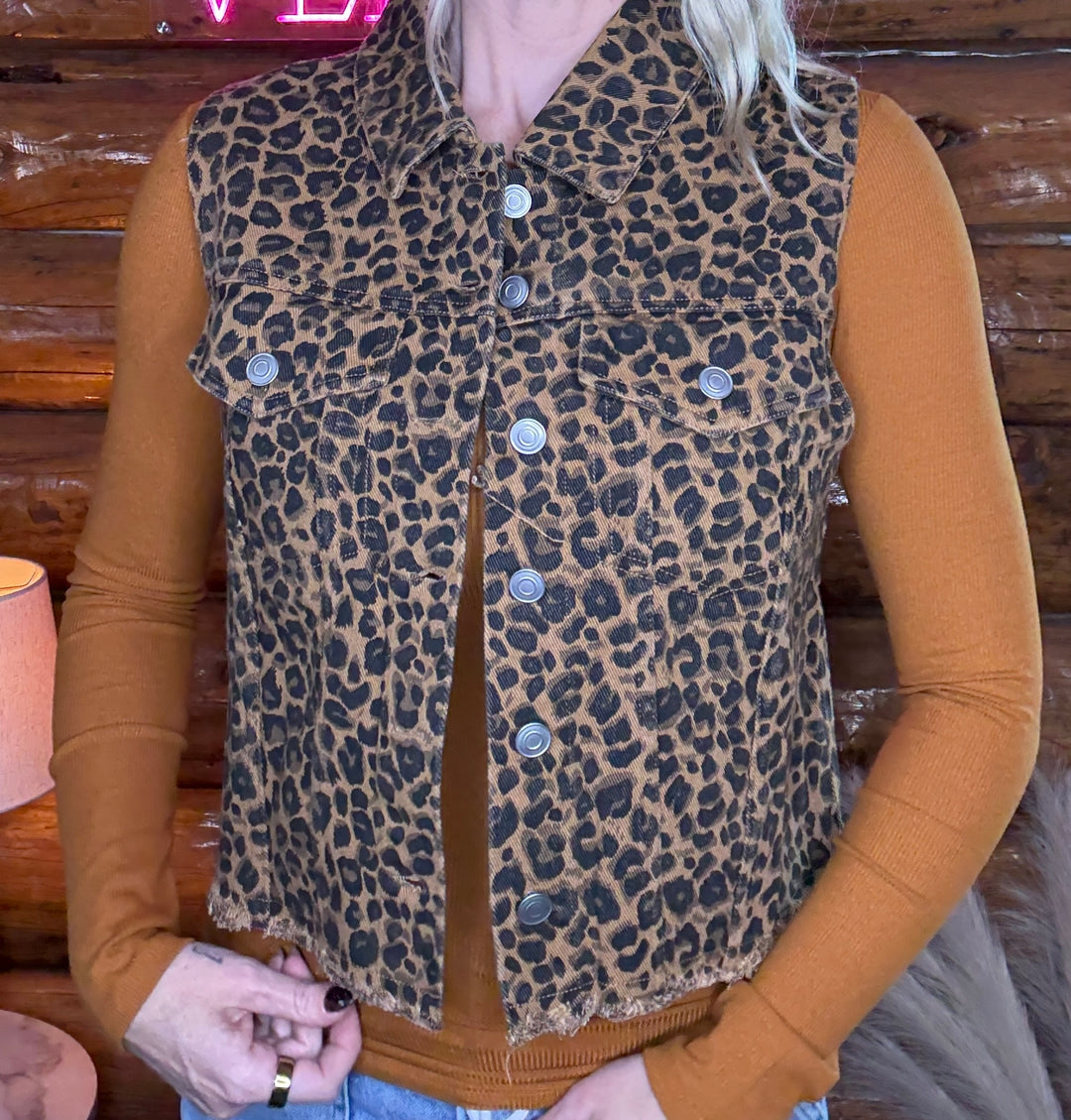 Person wearing a leopard print vest over a brown long-sleeve shirt with a wooden background.