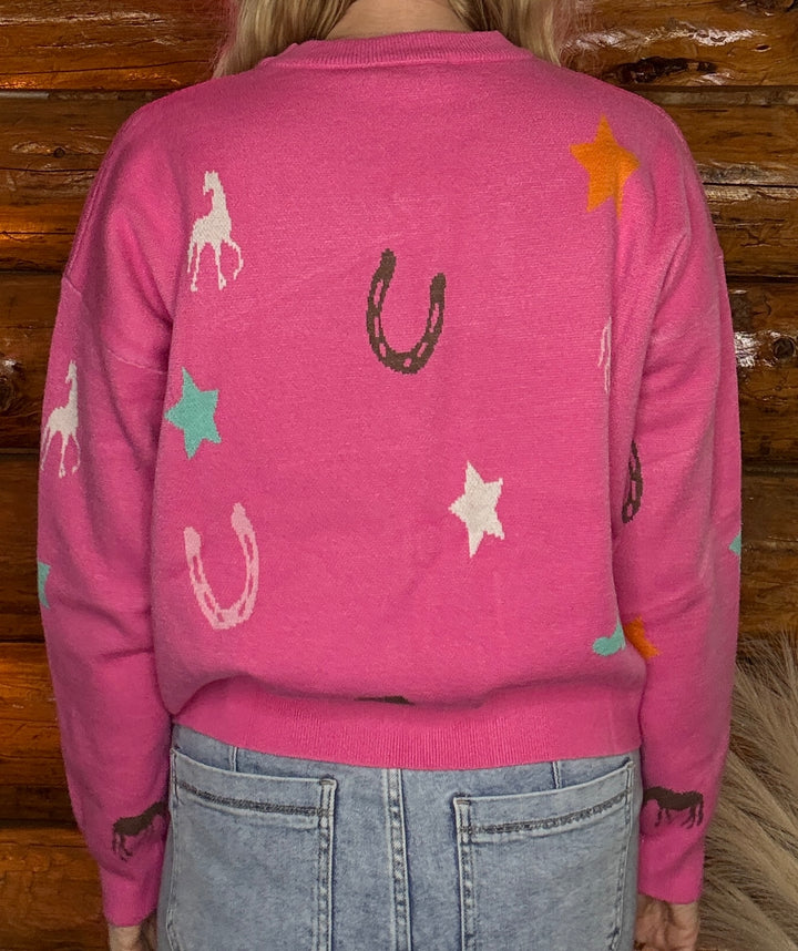 Pink sweater with horse and star patterns worn by a person against a wooden background