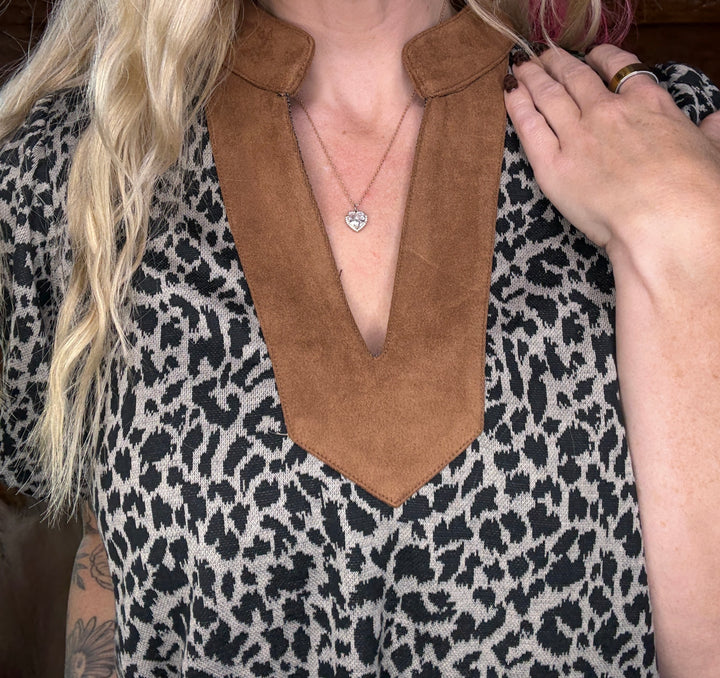 Person wearing a leopard print garment with a brown collar, held by a hand.