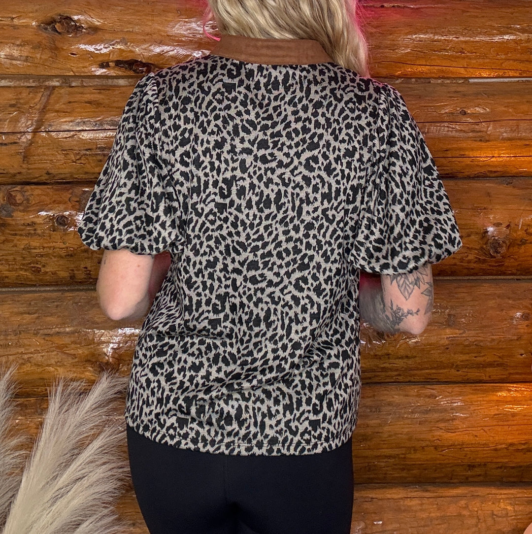 Person wearing a leopard print top against a wooden wall.