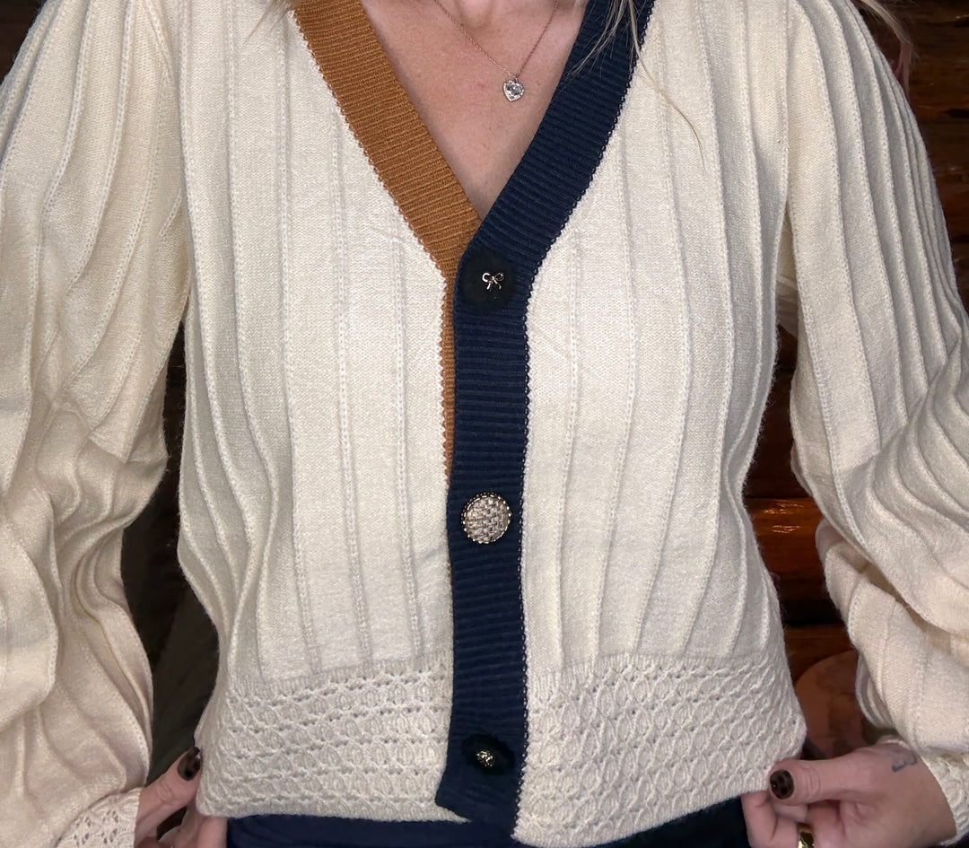 Close-up of a person wearing a white cardigan with brown and navy accents.
