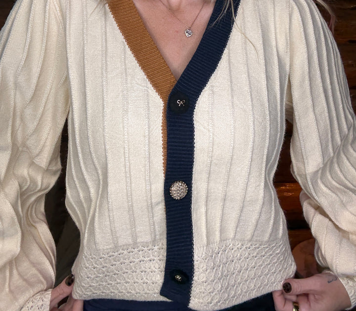 Close-up of a person wearing a white cardigan with brown and navy accents.