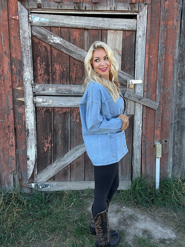 Woman wearing a jean barn jacket standing in front of a rustic wooden door