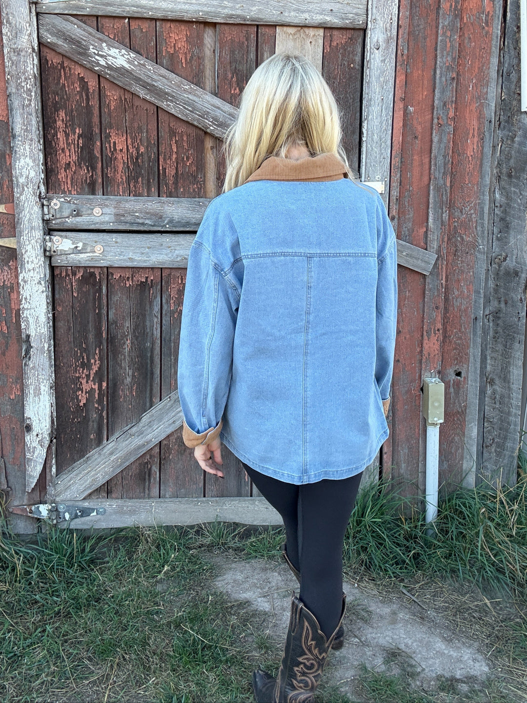 Person wearing a blue denim barn jacket standing in front of a rustic wooden door.