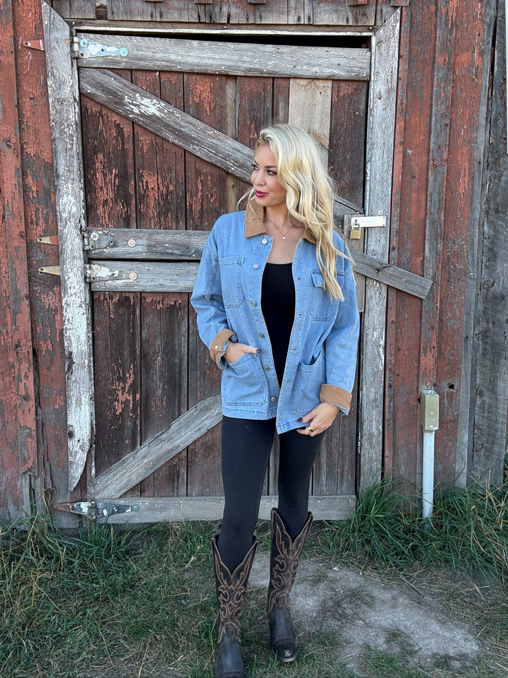 Woman wearing a denim barn jacket and cowboy boots standing in front of a rustic wooden door.