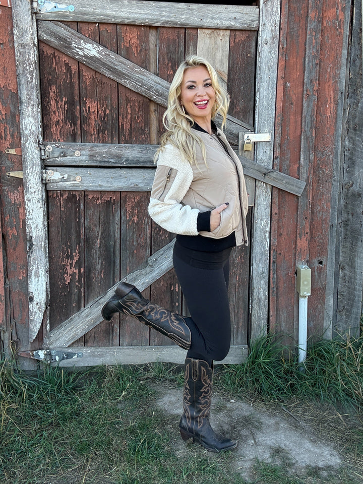 Woman wearing a 3 toned quilted bomber jacket posing in front of a rustic wooden barn door
