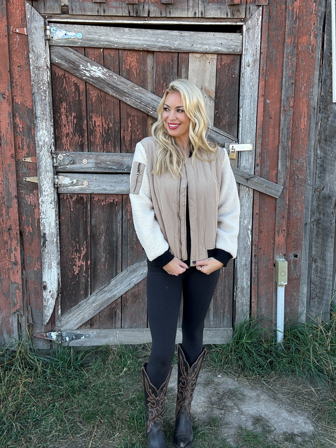 Woman wearing a 3 toned bomber jacket with quilted stitching standing in front of a rustic wooden door