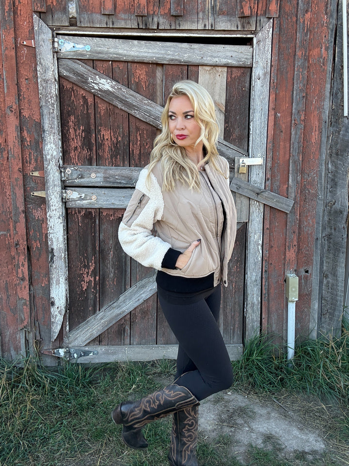 Woman wearing a 3 toned quilted bomber jacket standing in front of a rustic wooden door