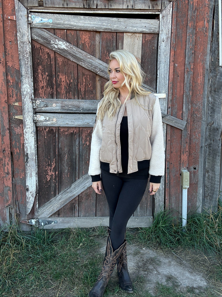 Woman wearing a 3 toned quilted bomber jacket standing in front of a rustic wooden door