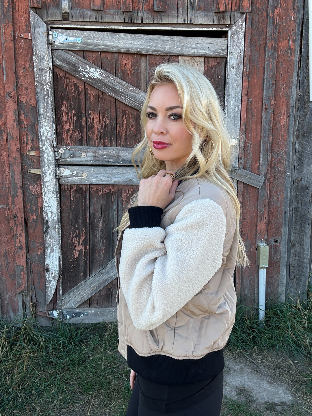 Woman wearing a 3 toned quilted bomber jacket standing in front of a rustic wooden door