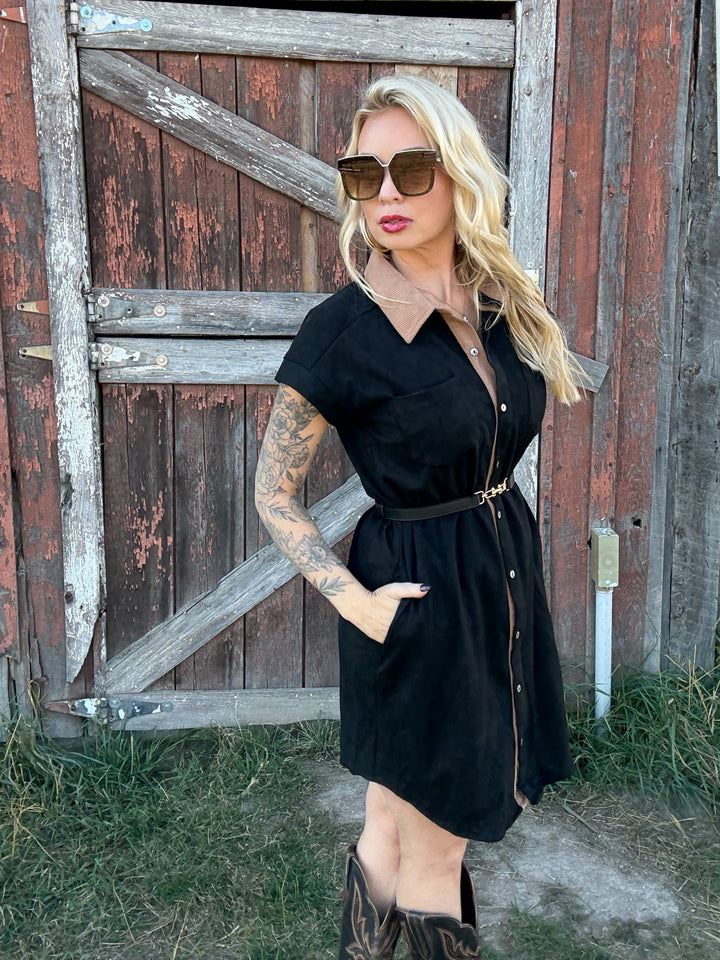 Woman in a black button up shirt dress standing in front of a rustic wooden door.
