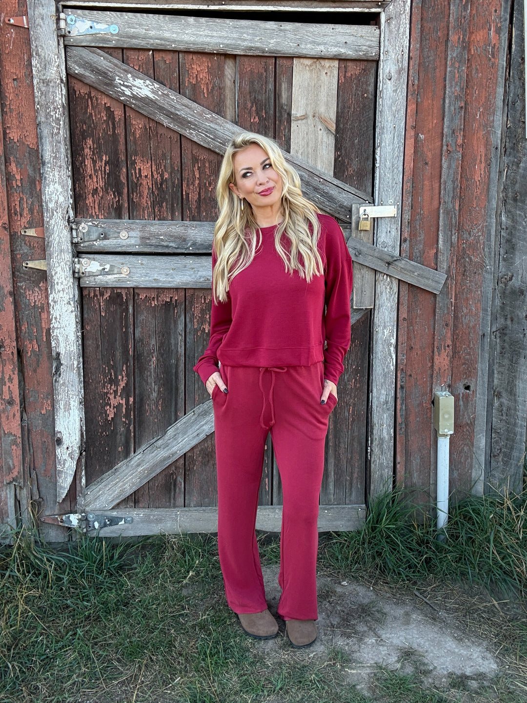 Woman in a red lounge outfit standing in front of a rustic wooden door.