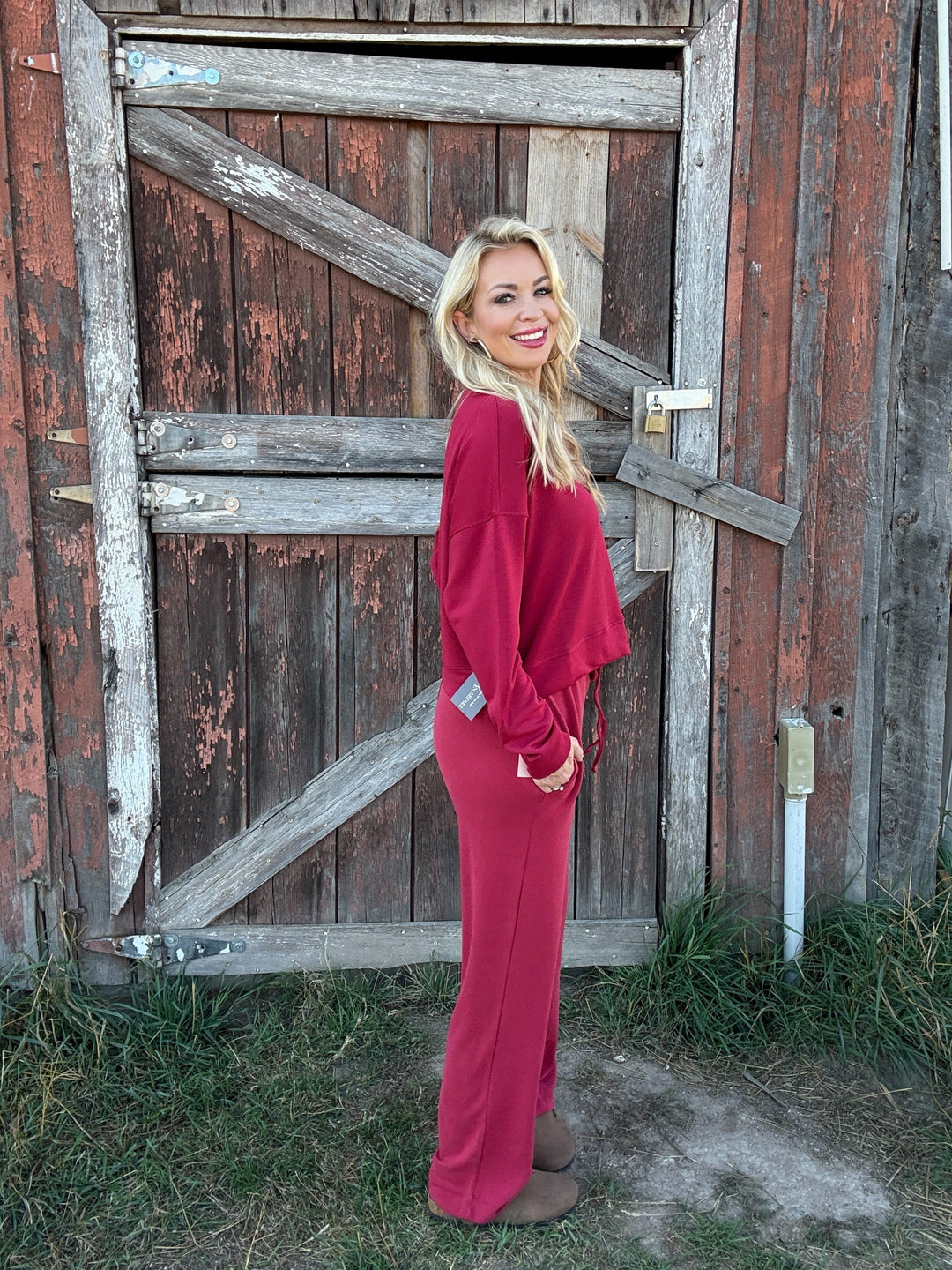 Woman in a red lounge outfit standing in front of a rustic wooden door.