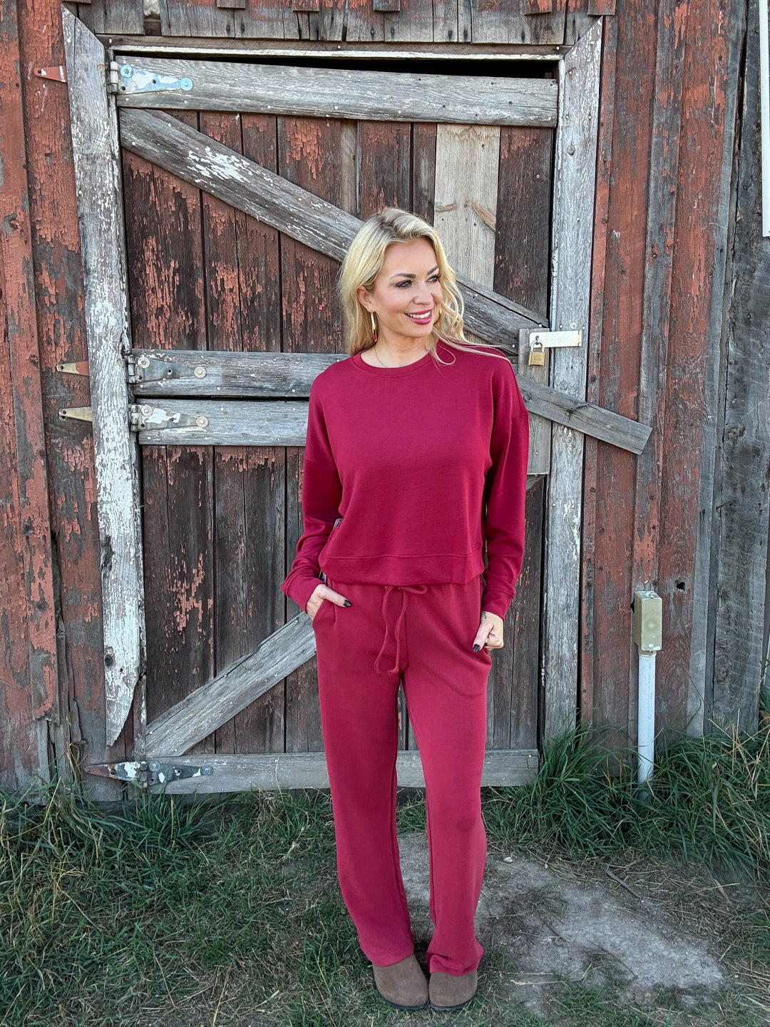 Woman in a red lounge outfit standing in front of a rustic wooden door.