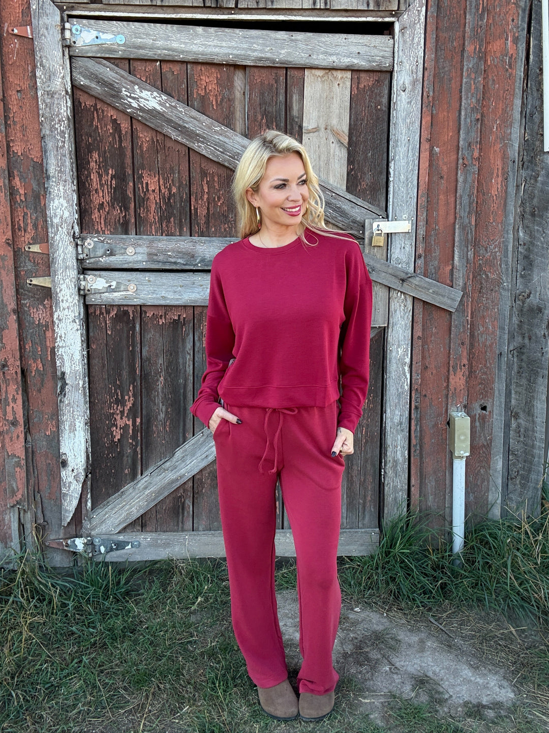 Woman in a red lounge outfit standing in front of a rustic wooden door.
