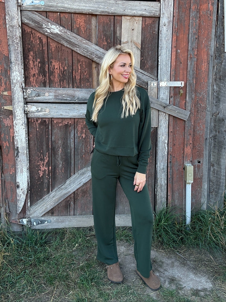 Woman in a green lounge outfit standing in front of a rustic wooden door.