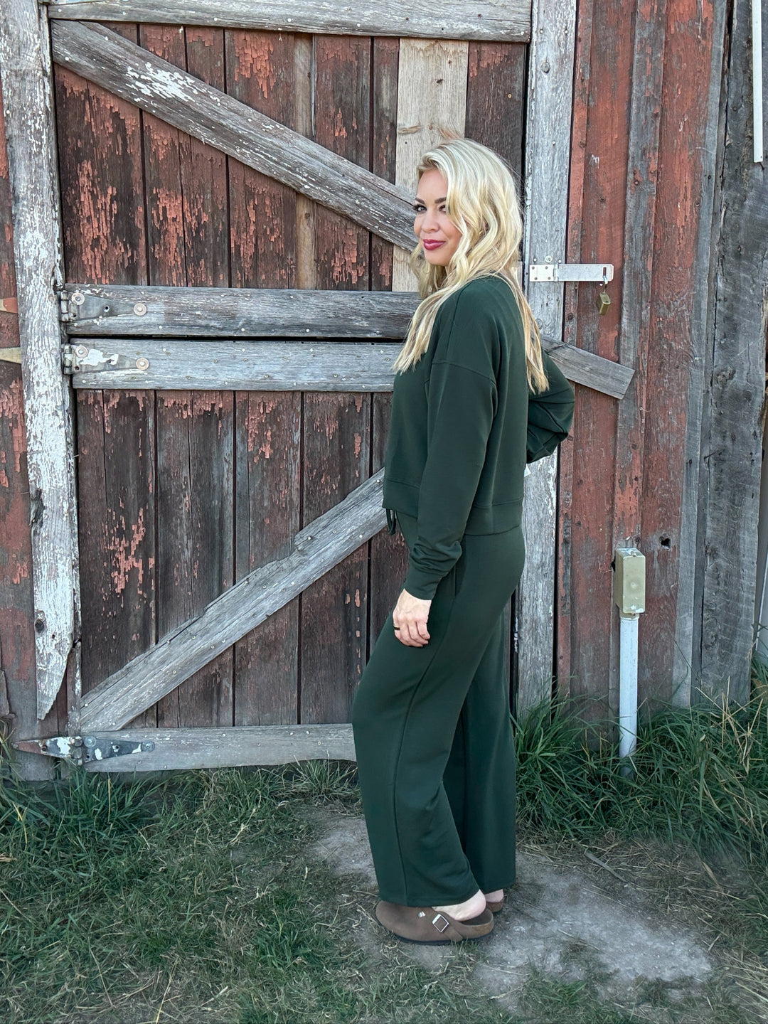 Woman in a green lounge outfit standing in front of a rustic wooden door.