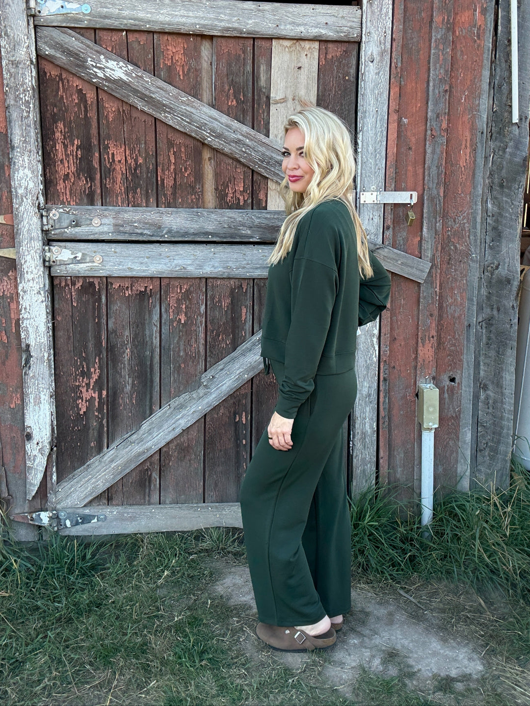 Woman in a green lounge outfit standing in front of a rustic wooden door.